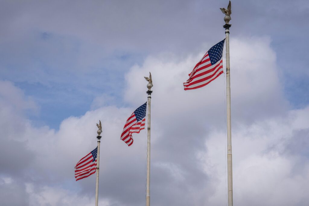 Three American flags waving against a backdrop of fluffy clouds, symbolizing national pride.
